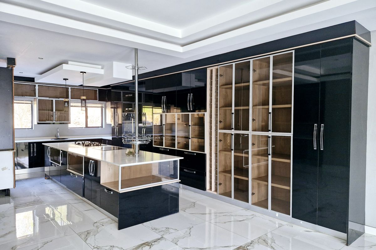 Modern, high-end kitchen featuring sleek black cabinetry, a large central island with stone countertop, glass-front display units, and polished marble-look floor tiles.