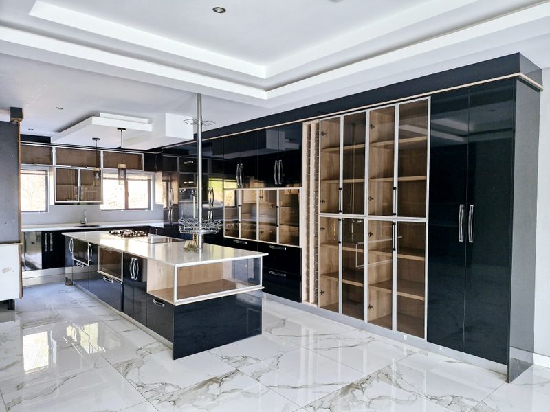 Modern, high-end kitchen featuring sleek black cabinetry, a large central island with stone countertop, glass-front display units, and polished marble-look floor tiles.