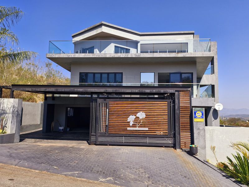 Modern multi-level residential facade featuring a contemporary sliding gate, paved driveway, carport, and glass balustrades on the upper balconies.