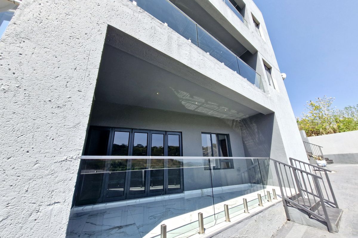 Modern rear exterior view featuring a covered patio with glass balustrades, marble-look tiling, and black aluminium folding doors leading into the home.