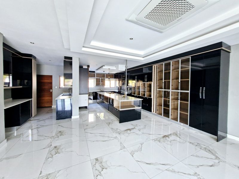 Modern, spacious kitchen featuring high-gloss black cabinetry, a large central island, marble-look tiled flooring, and integrated ceiling lighting.