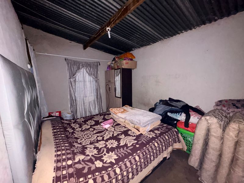 A bedroom featuring exposed timber beams and a corrugated iron roof with unfinished wall surfaces.