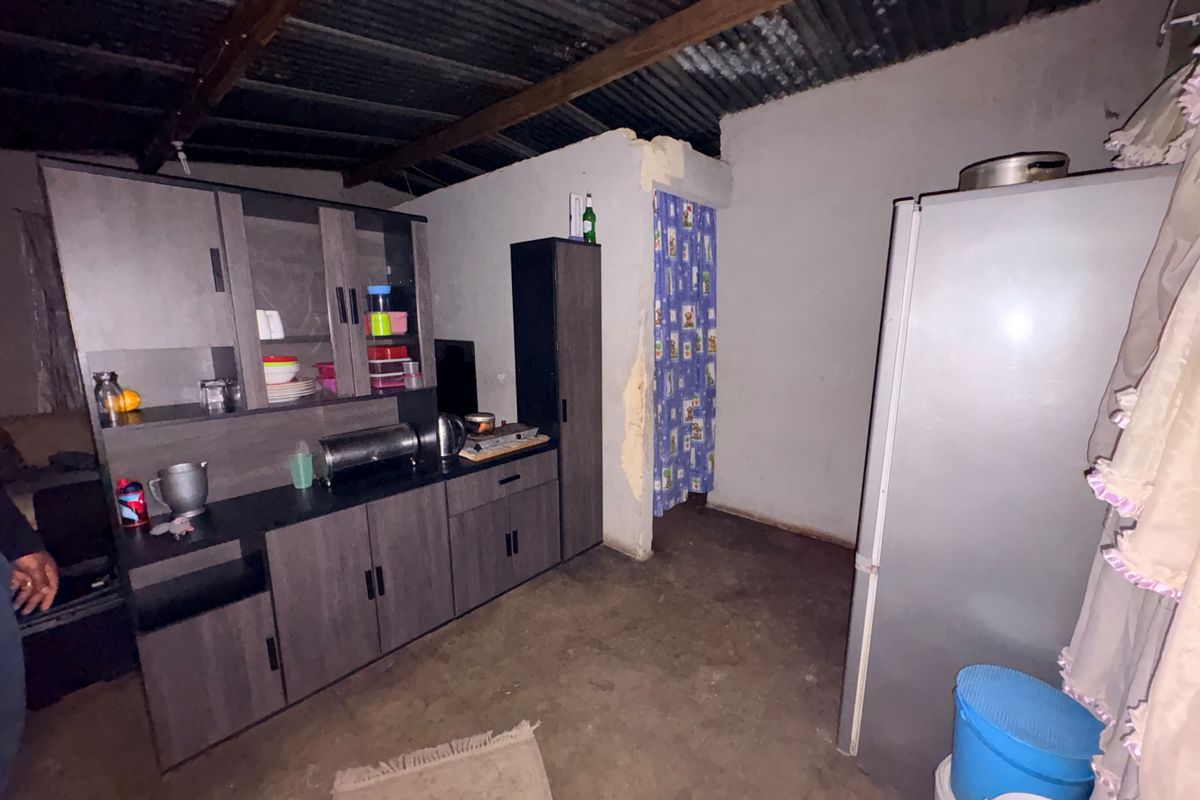 A basic kitchen area featuring built-in cabinetry, exposed timber rafters, and an unfinished corrugated metal ceiling with concrete flooring.