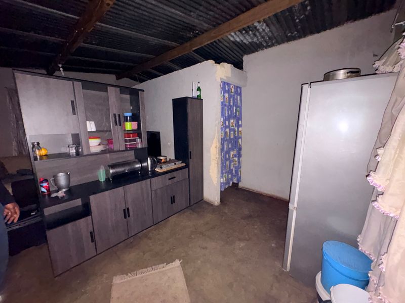A basic kitchen area featuring built-in cabinetry, exposed timber rafters, and an unfinished corrugated metal ceiling with concrete flooring.