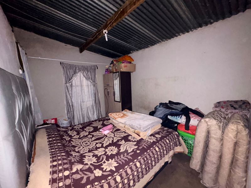 A basic bedroom featuring exposed corrugated iron roofing, timber beams, and plastered walls, requiring cosmetic updates to improve the living space.