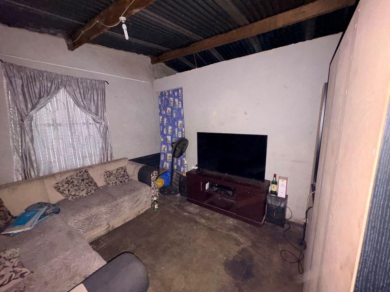 A living room space featuring exposed timber rafters and corrugated metal roofing, requiring significant renovation to improve finishes and overall condition.