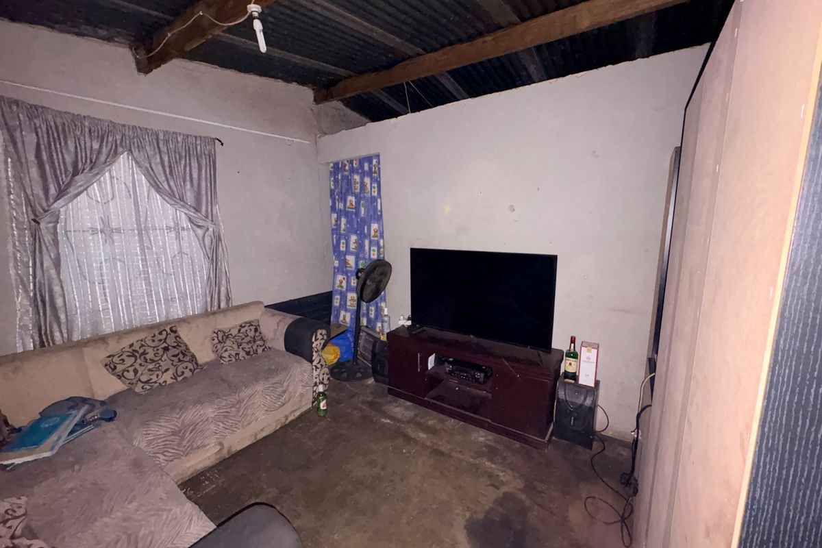 A living room featuring exposed timber rafters, corrugated metal ceiling, and unfinished wall surfaces, offering potential for renovation and modernization.