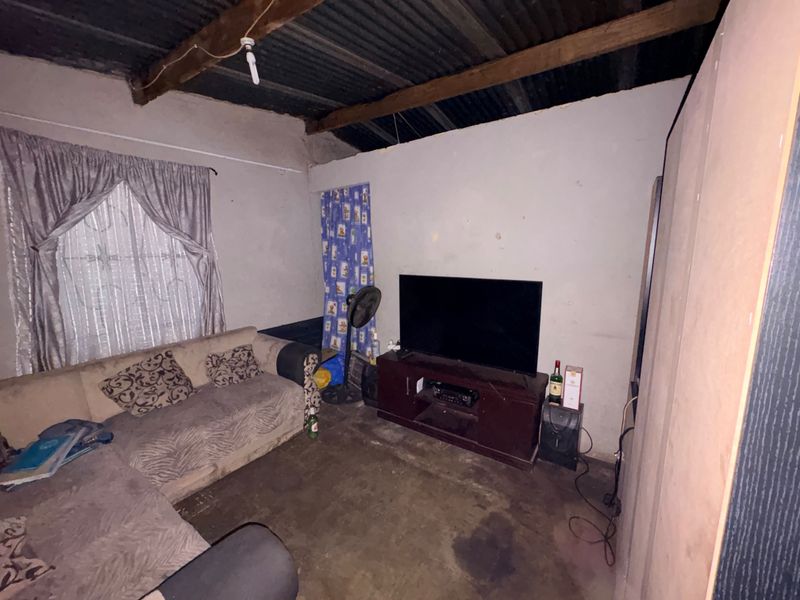 A living room featuring exposed timber rafters, corrugated metal ceiling, and unfinished wall surfaces, offering potential for renovation and modernization.