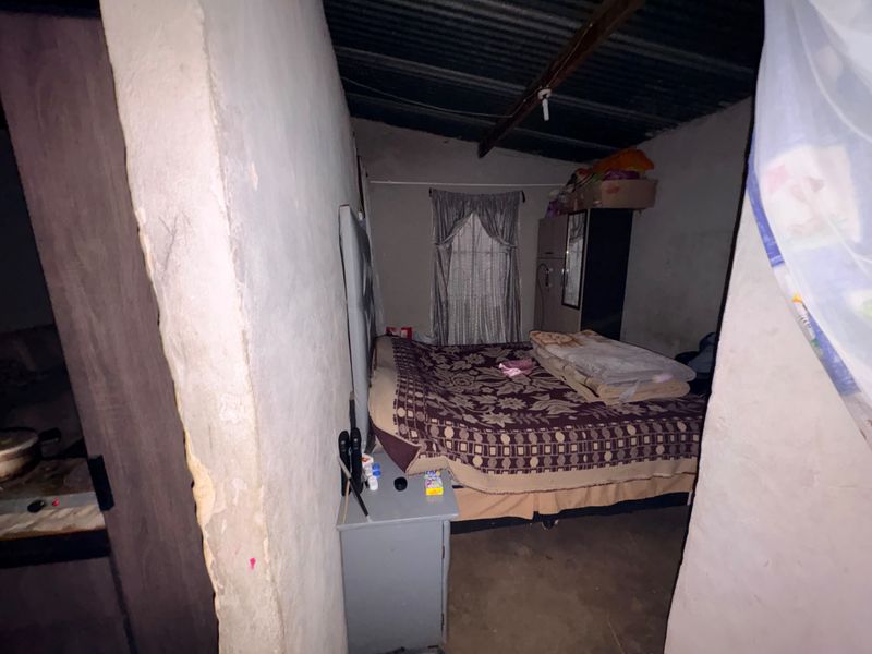 A basic bedroom featuring exposed roof rafters and unfinished wall surfaces, providing a functional sleeping space with potential for cosmetic improvement.