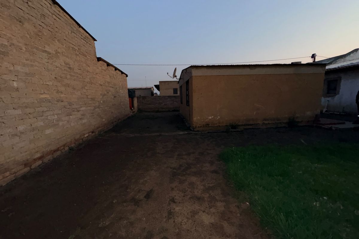 A view of the rear exterior area featuring exposed brick walls, a corrugated metal roof, and an unpaved yard space.