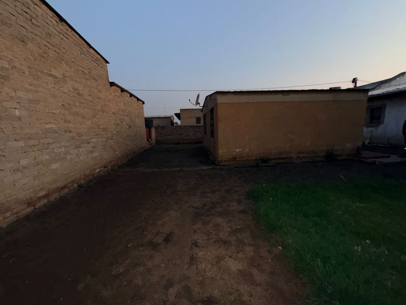 A view of the rear exterior area featuring exposed brick walls, a corrugated metal roof, and an unpaved yard space.