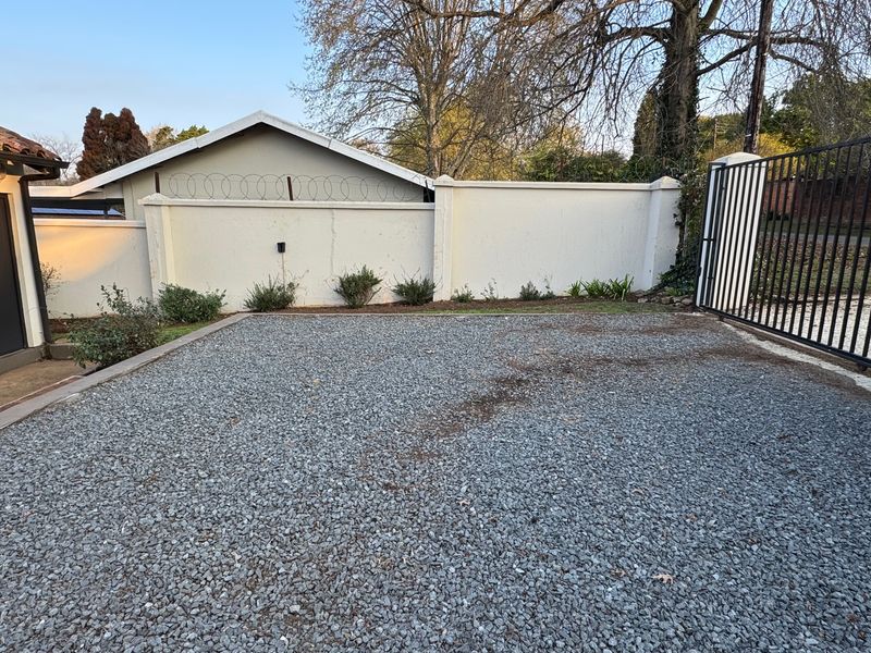 A gravel driveway area featuring a secure perimeter wall with razor wire and a metal entrance gate.