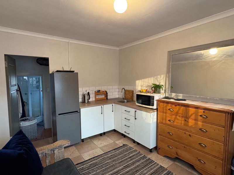Compact kitchen area featuring white cabinetry, subway tile backsplash, laminate countertops, and tiled flooring, with an adjacent doorway leading to a bathroom.