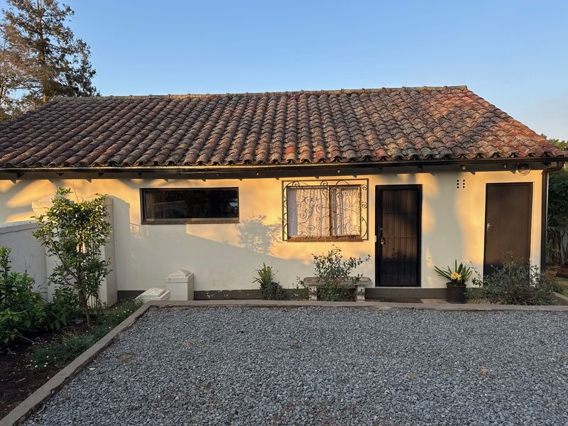 Rear exterior view of a cottage featuring a terracotta tiled roof, plastered walls, and a gravel courtyard area.