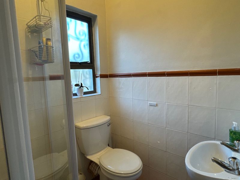A compact bathroom featuring a shower enclosure, pedestal basin, and toilet with dated wall tiling and a frosted glass window.