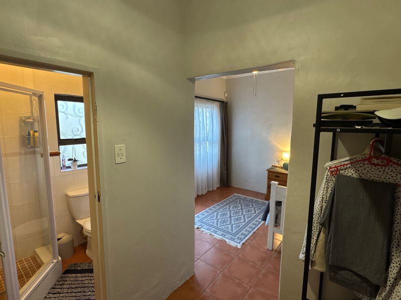A view from a hallway looking into a bathroom with a shower and a bedroom with tiled flooring.