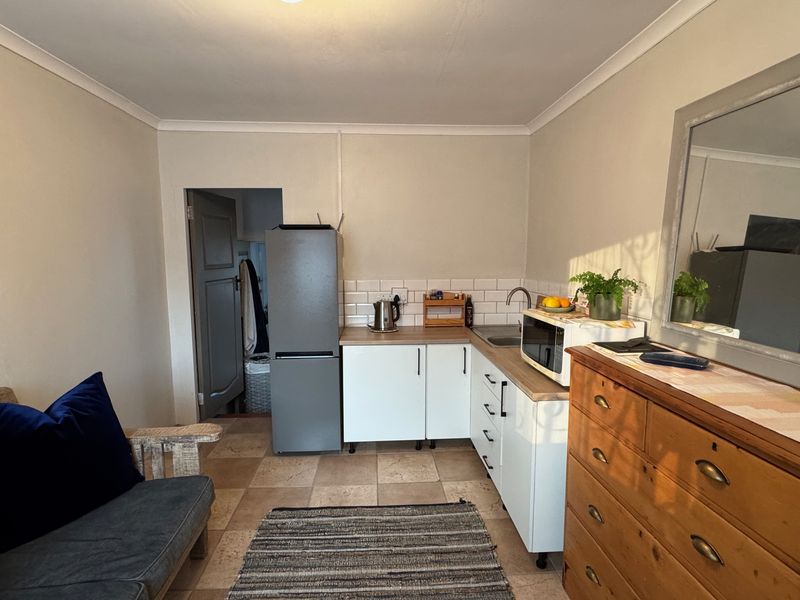 A compact kitchen area featuring white cabinetry, a subway tile backsplash, and tiled flooring, providing a functional prep space within the cottage.