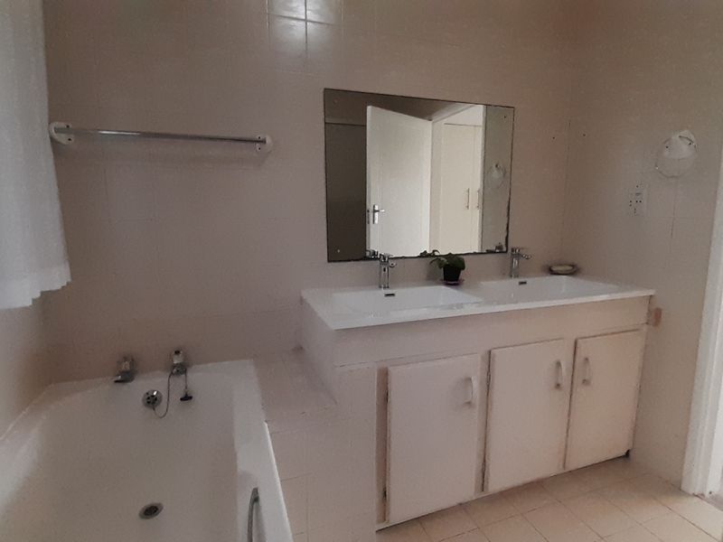 A functional bathroom featuring a double vanity with built-in cabinetry, a bathtub, and neutral wall and floor tiling.