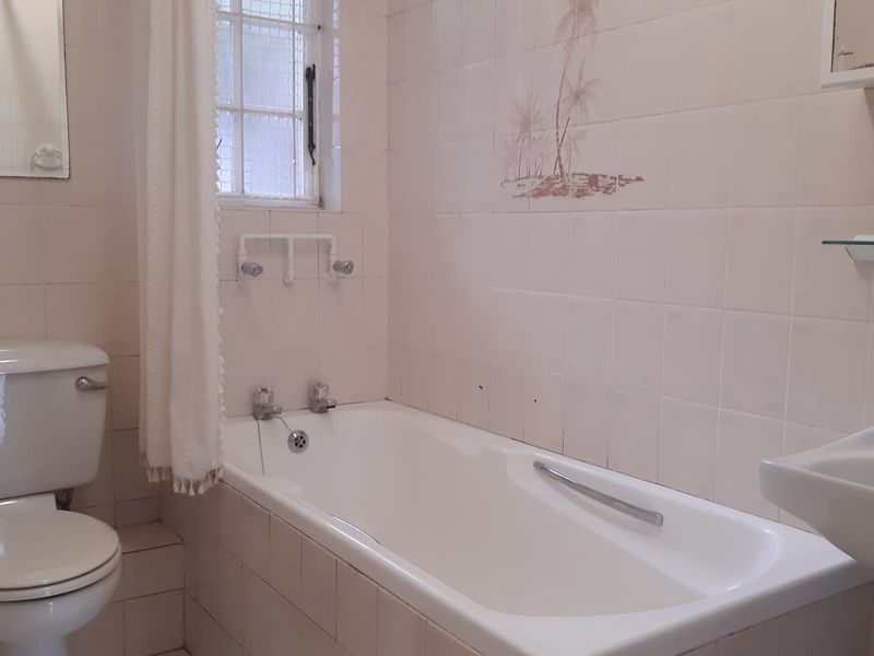 A dated bathroom featuring a standard bathtub, toilet, and washbasin with original wall tiling.