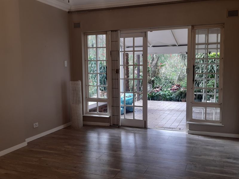 An empty living room featuring laminate flooring and large french doors that open onto a paved patio area.