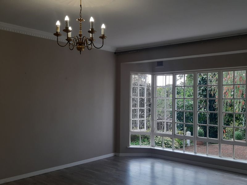Spacious living room featuring large bay windows with security bars, laminate flooring, and elegant crown molding with a central ceiling rose.