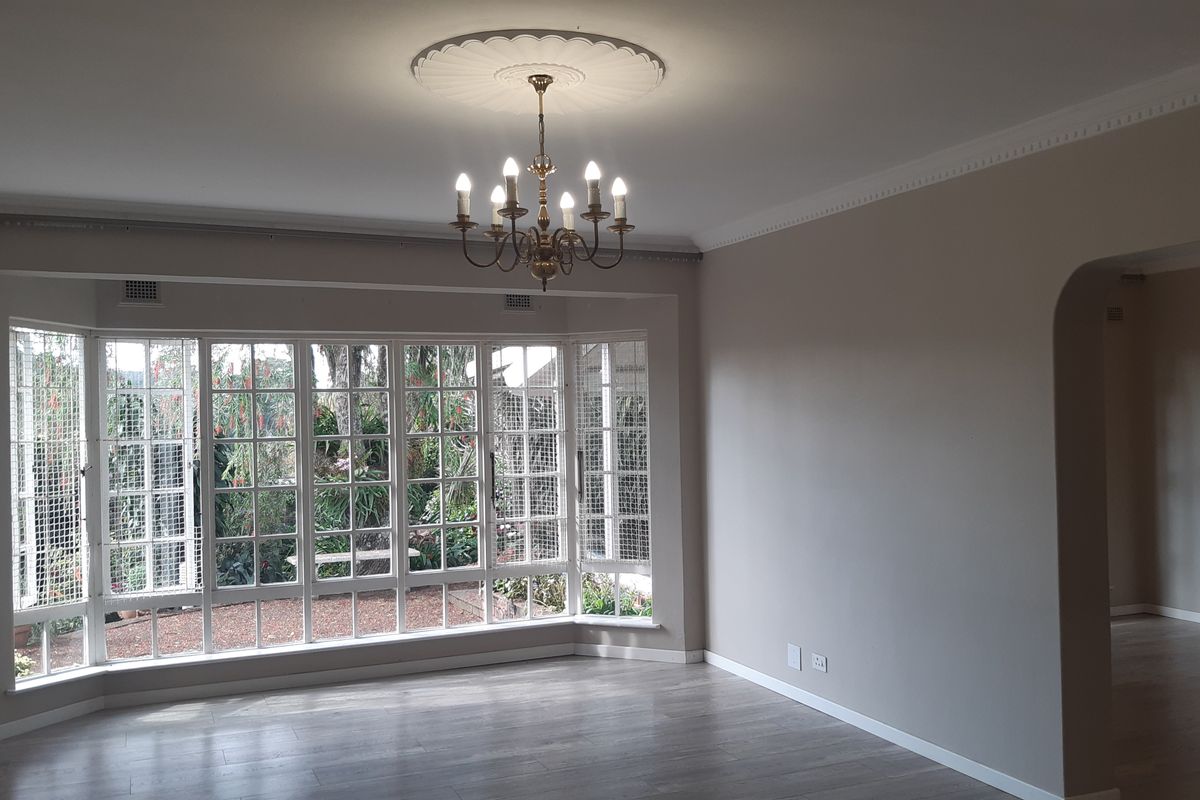 Spacious living room featuring a large bay window, elegant ceiling rose with chandelier, and modern laminate flooring, offering a bright and neutral living space.