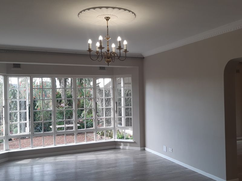 Spacious living room featuring a large bay window, elegant ceiling rose with chandelier, and modern laminate flooring, offering a bright and neutral living space.