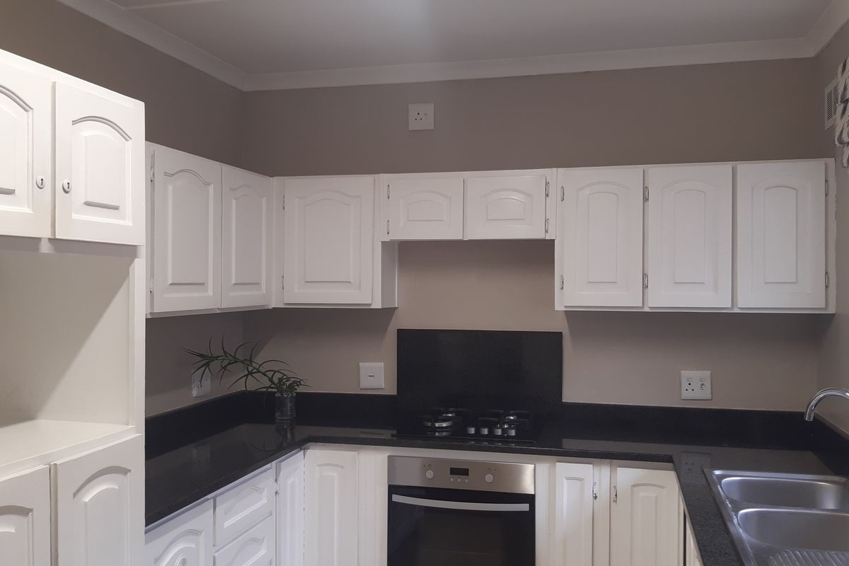 A clean, functional kitchen featuring white cabinetry, black granite countertops, a built-in oven, gas hob, and a stainless steel sink.