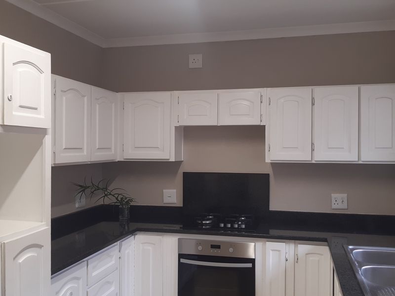 A clean, functional kitchen featuring white cabinetry, black granite countertops, a built-in oven, gas hob, and a stainless steel sink.