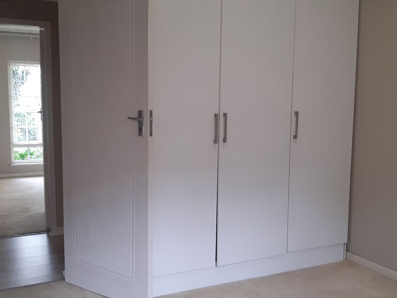 A bedroom featuring a large built-in wardrobe with white cabinetry and neutral carpet flooring, with a view into an adjacent hallway.