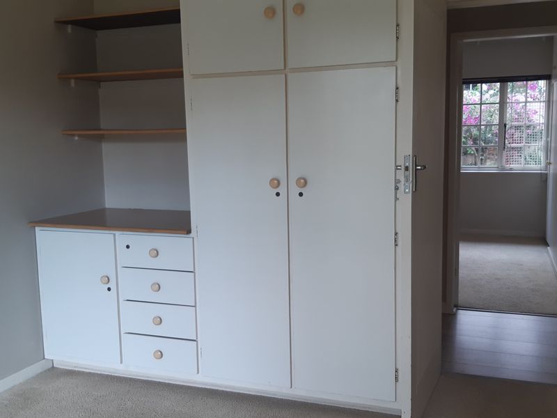 A bedroom featuring built-in cupboards with integrated shelving and a desk area, finished with neutral wall tones and carpeted flooring.
