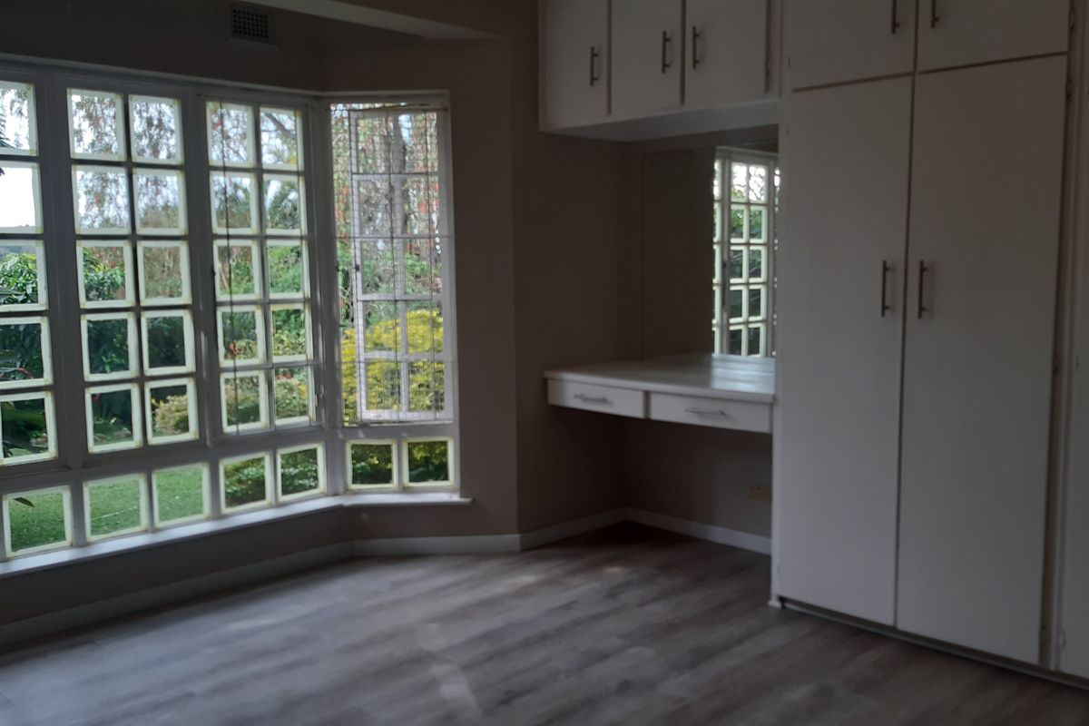 Spacious bedroom featuring a large bay window, built-in cupboards, and a integrated vanity area with modern laminate flooring.