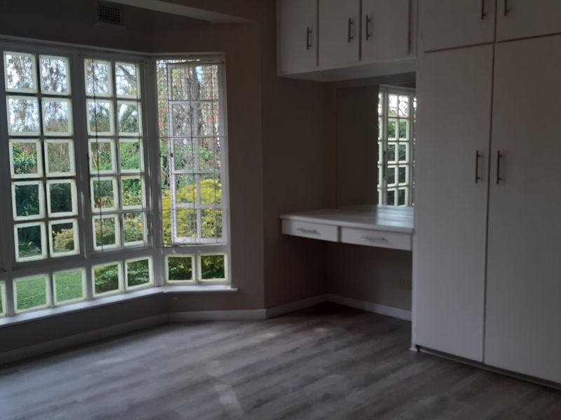 Spacious bedroom featuring a large bay window, built-in cupboards, and a integrated vanity area with modern laminate flooring.