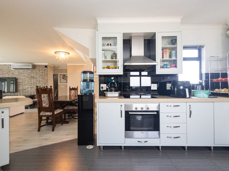 Open-plan kitchen and living area featuring modern cabinetry, integrated appliances, stone countertops, and a stylish stone feature wall with air conditioning.