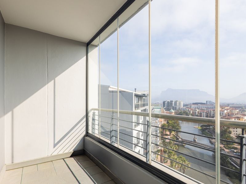 A modern enclosed balcony featuring frameless glass panels, a metal balustrade, and tiled flooring, offering expansive views of the surrounding estate and mountains.