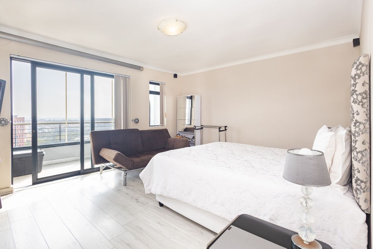 Spacious bedroom featuring light laminate flooring and large sliding glass doors providing access to a private balcony with city views.