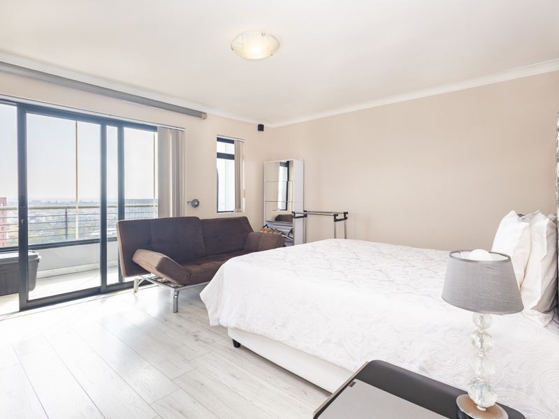Spacious bedroom featuring light laminate flooring and large sliding glass doors providing access to a private balcony with city views.