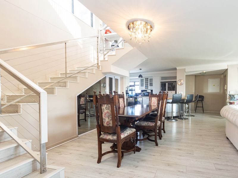 Spacious open-plan living and dining area featuring a modern staircase with stainless steel balustrades, light laminate flooring, and an integrated kitchen breakfast bar.