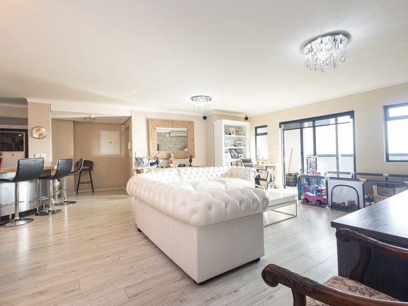 Spacious open-plan living area featuring light laminate flooring, modern crystal chandeliers, and large sliding glass doors leading to a balcony.