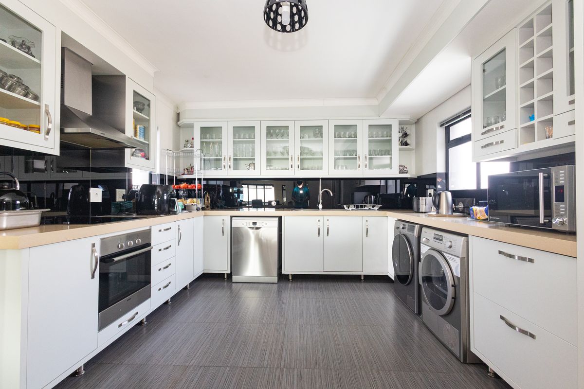 Modern kitchen featuring white cabinetry, glass-fronted display units, integrated appliances, dark tiled flooring, and a sleek black splashback.
