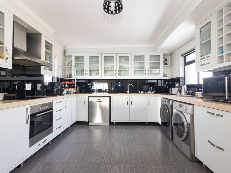 Modern kitchen featuring white cabinetry, glass-fronted display units, integrated appliances, dark tiled flooring, and a sleek black splashback.