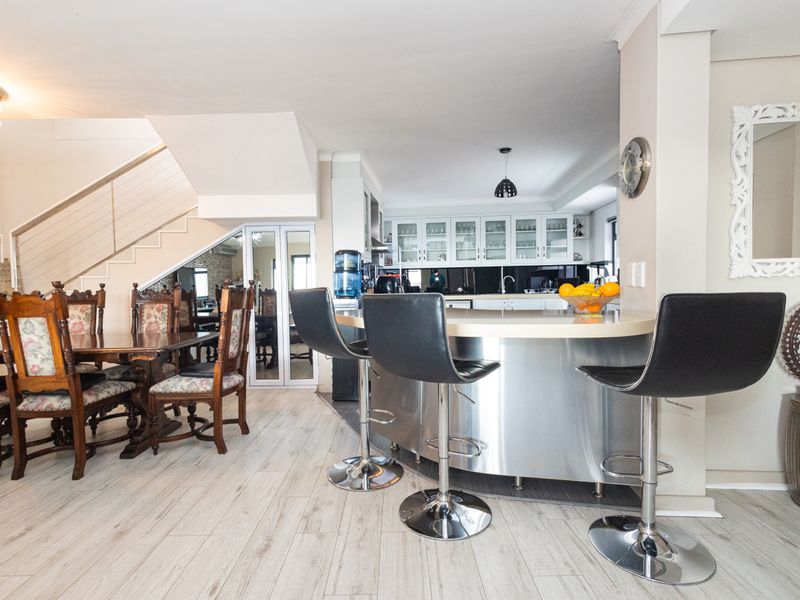 Open-plan living area featuring a modern kitchen with stainless steel breakfast bar, glass-fronted cabinetry, and a staircase leading to the upper level.