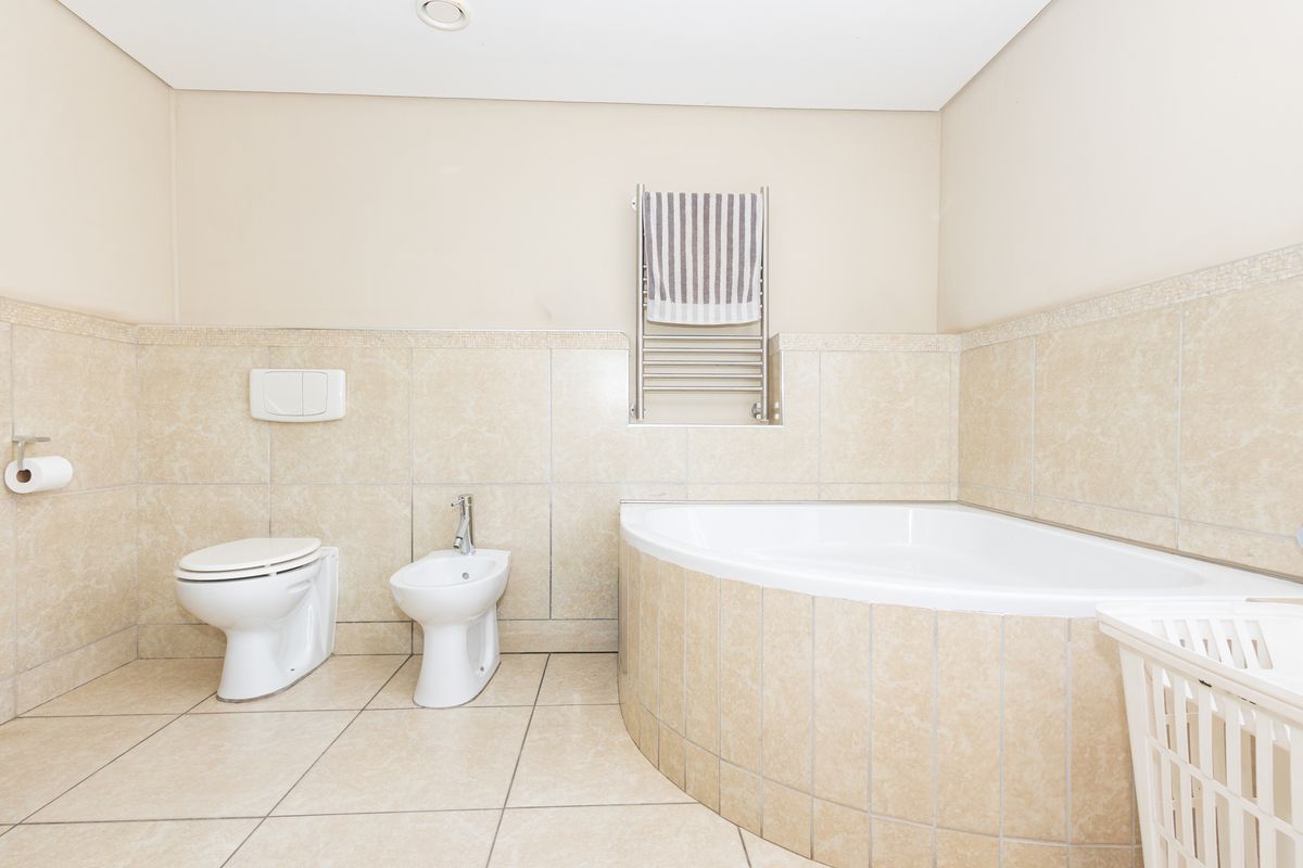 A well-maintained bathroom featuring a corner bathtub, wall-mounted toilet, bidet, and a heated towel rail with neutral tiled finishes.