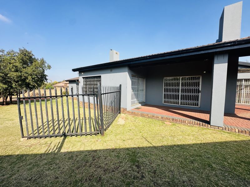 Rear view of the property featuring a covered patio with brick paving, secure metal gates, and a well-maintained lawn area.