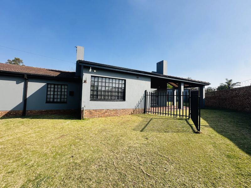 Rear view of the house featuring a grey rendered facade, brick base, covered patio area, and a secure metal gate leading to the garden.