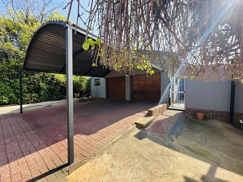 Exterior view of a double garage with wooden doors, a covered carport, and a paved driveway area.