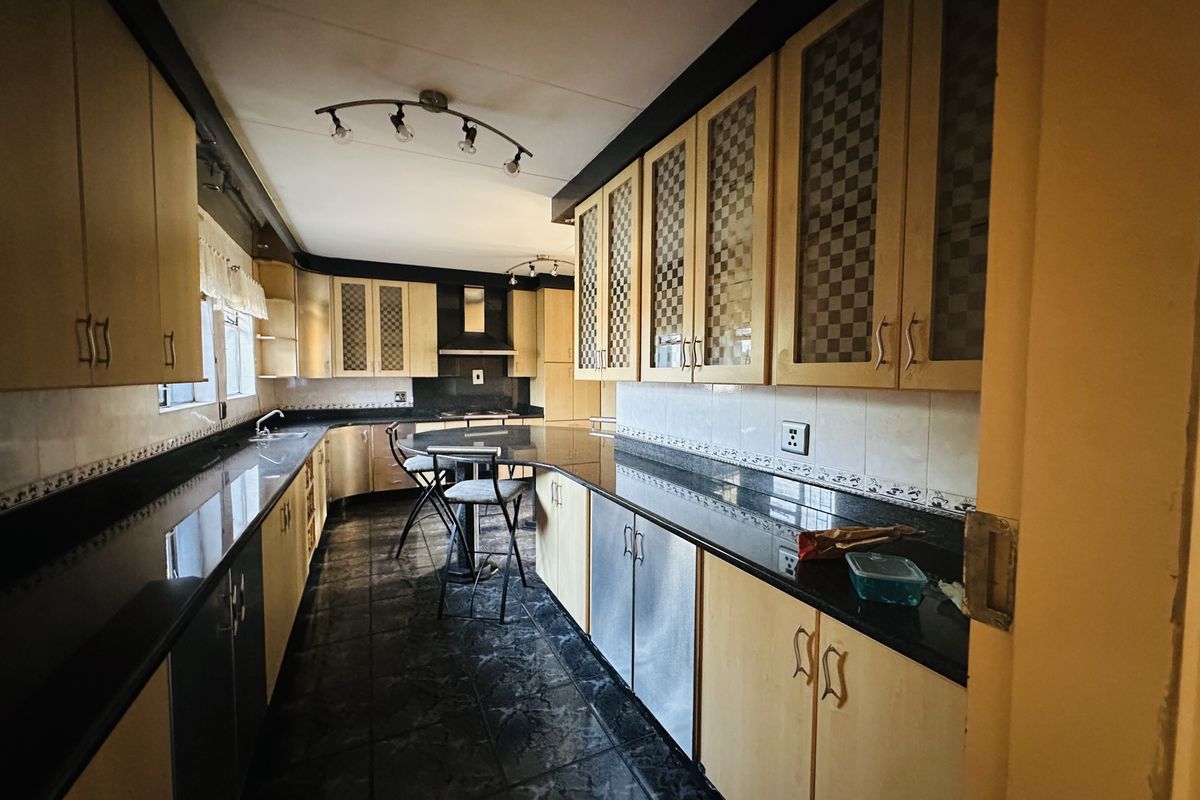 A spacious kitchen featuring extensive granite countertops, ample built-in cabinetry, a dedicated extractor fan, and dark tiled flooring.