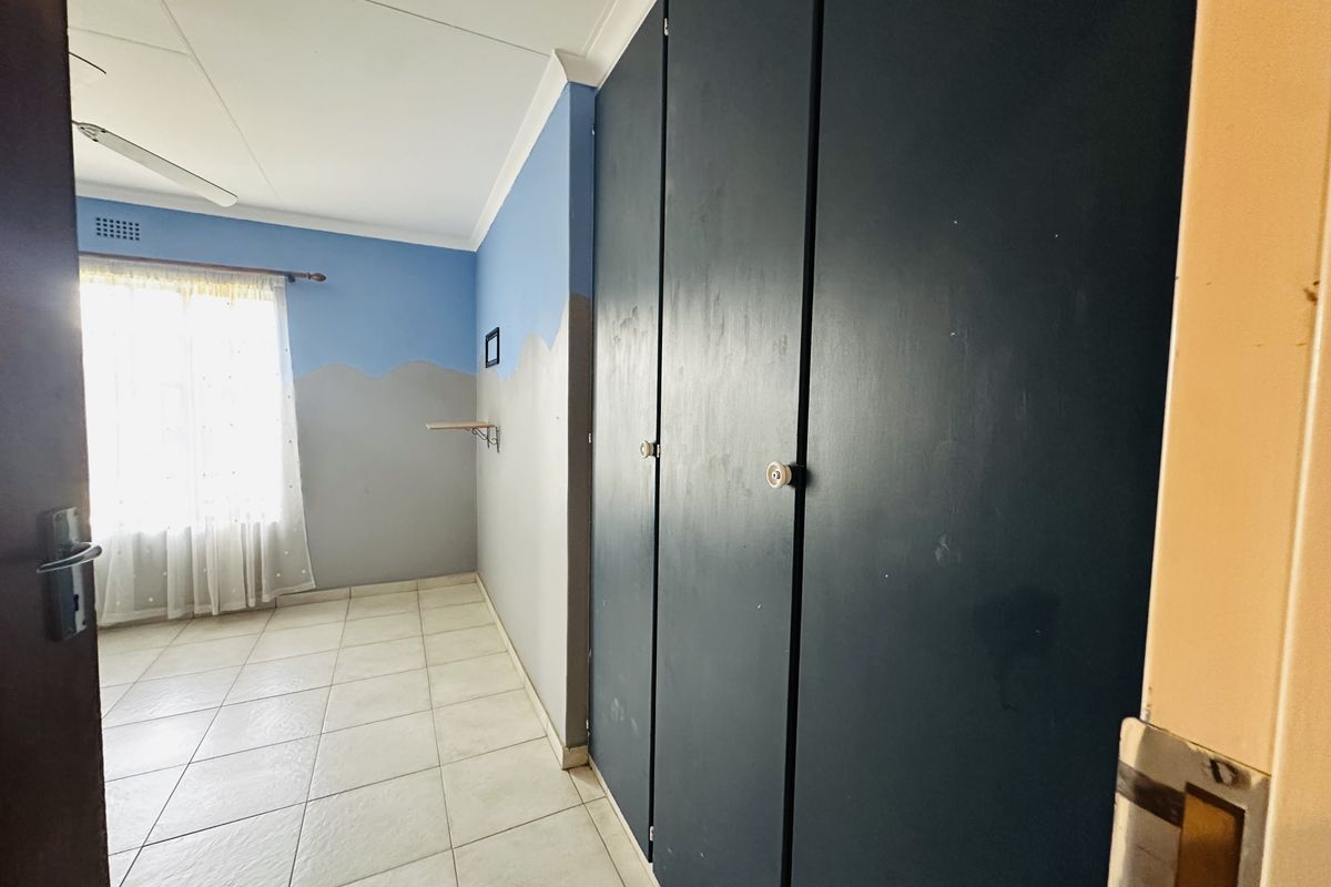 A bedroom featuring tiled flooring, a ceiling fan, and dark built-in cupboards, offering a blank canvas for potential interior updates.