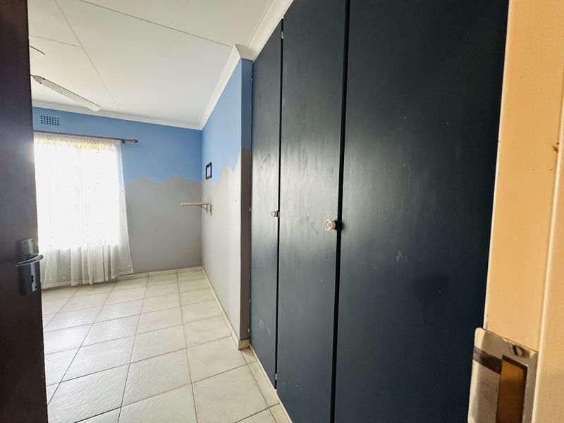 A bedroom featuring tiled flooring, a ceiling fan, and dark built-in cupboards, offering a blank canvas for potential interior updates.