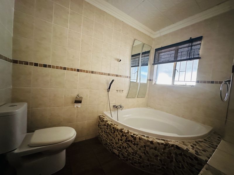 A functional bathroom featuring a built-in bathtub with stone-tiled surround, a standard toilet, and neutral wall tiling.